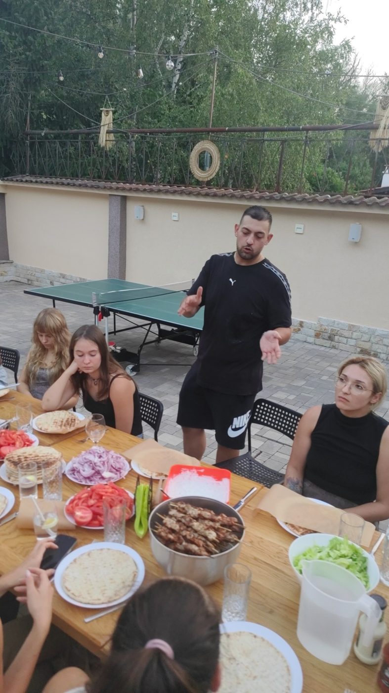 A member of the Greek team talks the group through the dinner, with skewers and pitas on the table