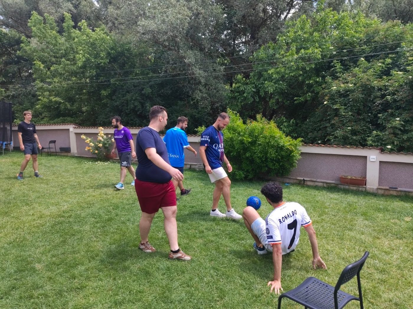 A participant in a Ronaldo 7 shirt controls the ball while sitting on the grass as others watch