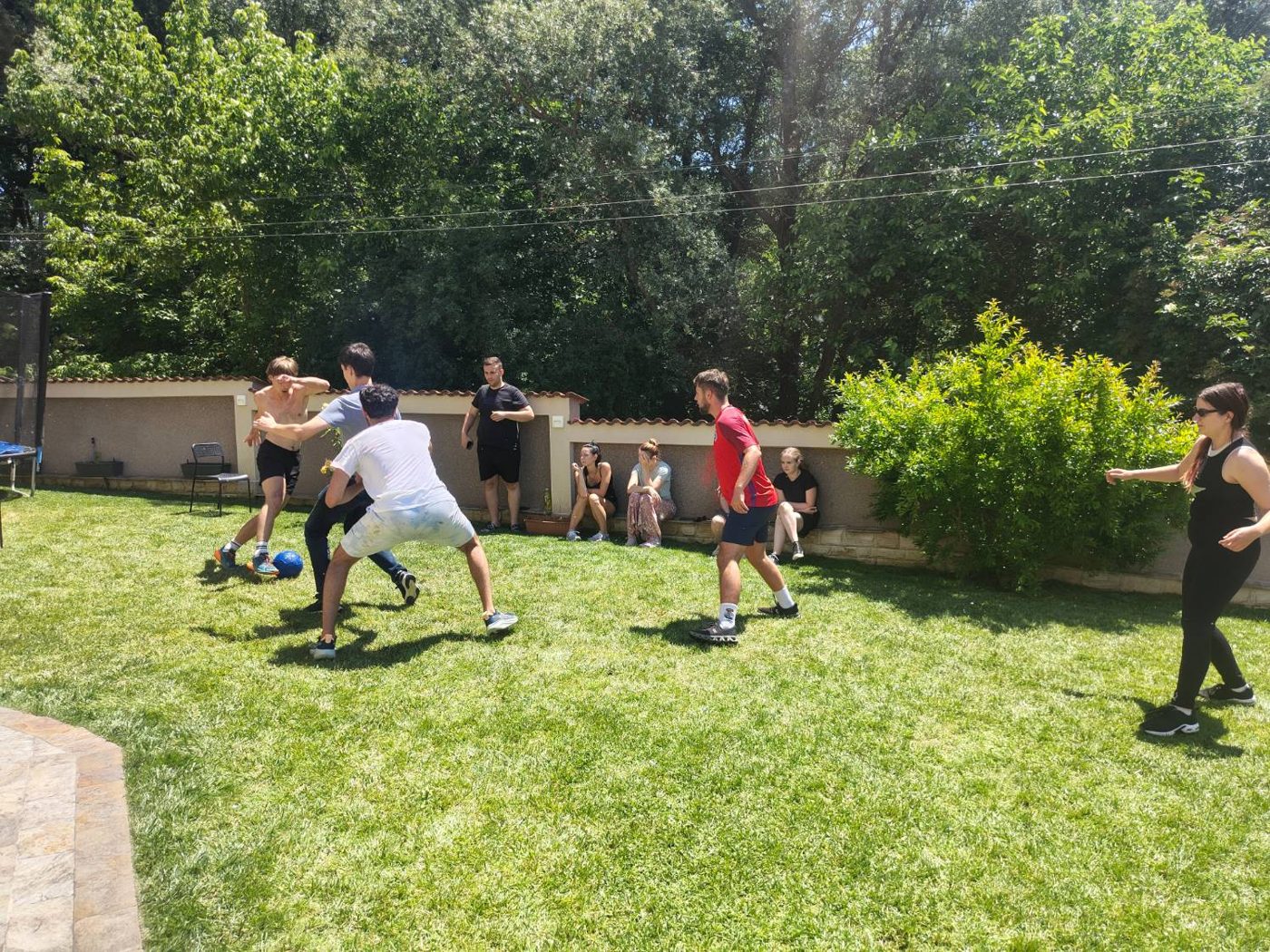 A lively tackle for the ball during a garden match, with teammates cheering from the side