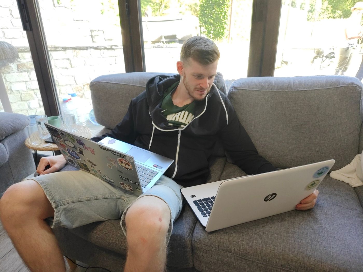A participant works on two laptops at once on the sofa